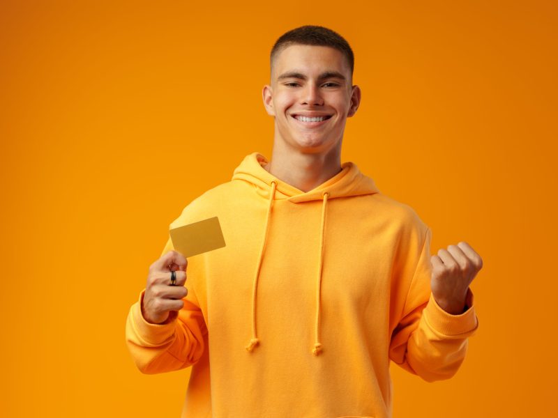 Young handsome man over yellow background holding a credit card in studio
